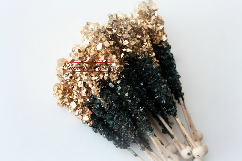 May include: A bunch of black and gold rock candy sticks on wooden sticks. The candy is in the shape of crystals.