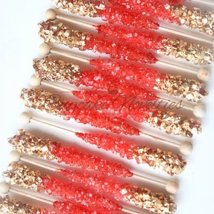 May include: Red and gold rock candy sticks on wooden sticks. The candy is in a swirl pattern with red on top and gold on the bottom.