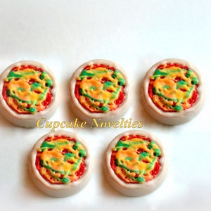 May include: Five mini pizza cupcakes decorated with red, yellow, and green frosting. The cupcakes are arranged in a circle on a white surface. Cupcake Novelties is written in the center of the image.