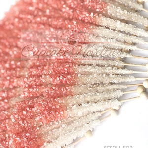 May include: A close-up of a bunch of pink and white rock candy sticks on wooden sticks. The candy sticks are arranged in a fan shape. The text "SCROLL FOR MORE PICTURES" is at the bottom of the image.