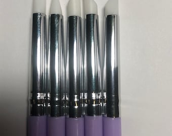 May include: A set of five sculpting tools with light purple handles and silver metal ferrules. Each tool features a distinct white silicone tip in various shapes, including flat, pointed, angled, and rounded edges for precise shaping and detailing.