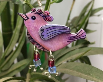 May include: Pink and purple bird earring with blue and silver accents. The bird has a detailed design and is hanging from a silver wire.