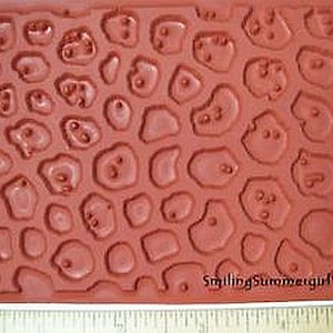 Puede incluir: Un sello de goma rojo con un patrón de círculos en relieve, que se asemeja a un estampado de leopardo. El sello está etiquetado como "SmilingSummergirl".
