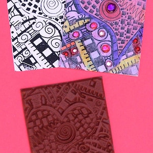 Puede incluir: Un primer plano de un sello de goma con un diseño en forma de corazón. El sello es marrón y tiene un patrón detallado de cuadrados, círculos y líneas. El texto "Somethings Fishy Rubber Stamp" está impreso debajo del sello.