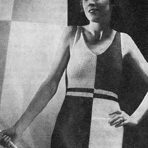May include: Black and white knitted swimsuit with a geometric pattern. The swimsuit has a scoop neck and a wide, contrasting band around the waist. The model is wearing the swimsuit and has her hand on her hip.