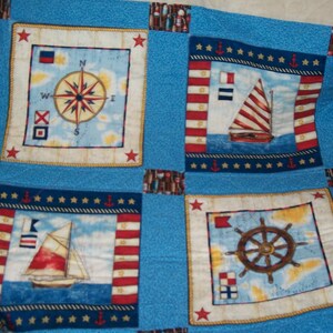 May include: A blue and white nautical themed quilt with four squares. Each square features a different nautical design: a compass, a sailboat, a ship's wheel, and a sailboat with a red, white and blue striped sail.