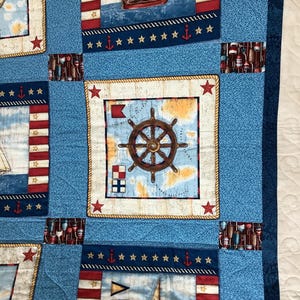 May include: A blue and white nautical themed quilt with a red, white and blue striped pattern. The quilt features a compass, a ship's wheel, and a sailboat.