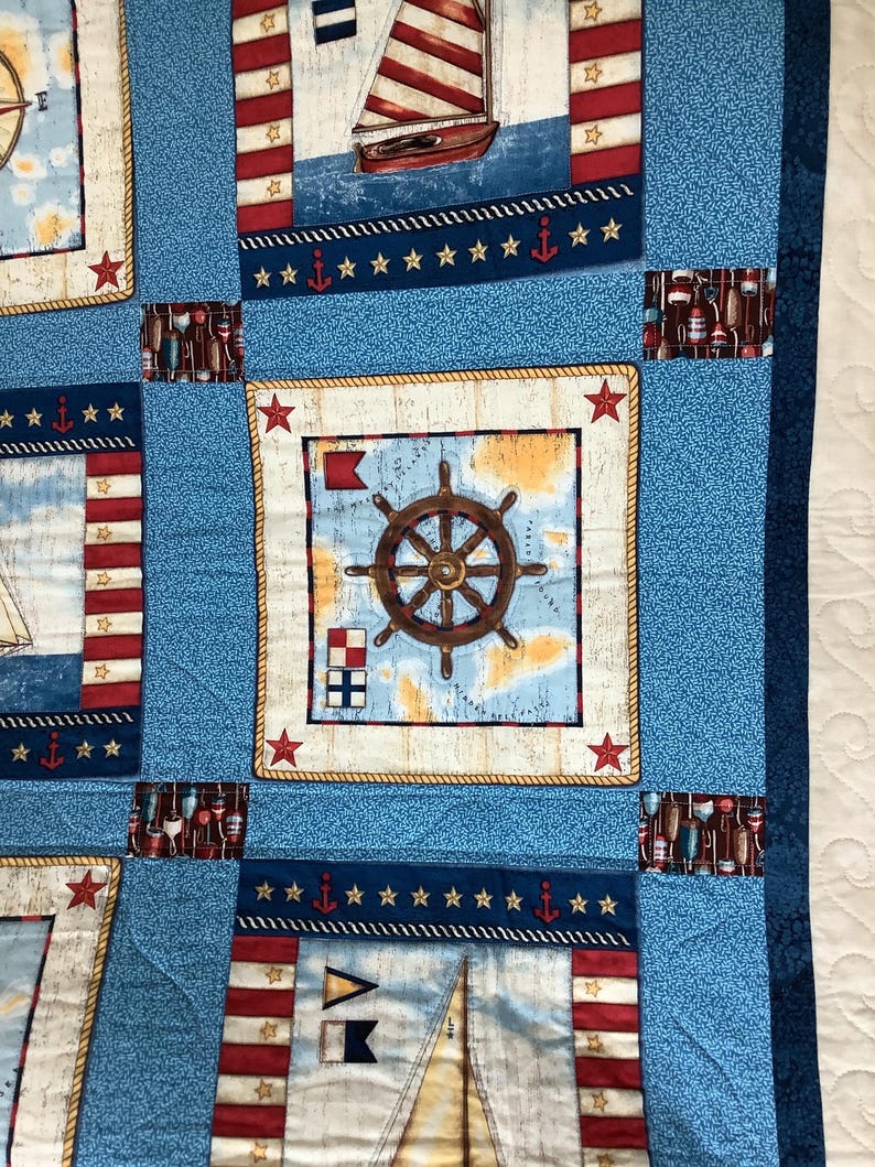 May include: A blue and white nautical themed quilt with a red, white and blue striped pattern. The quilt features a compass, a ship's wheel, and a sailboat.
