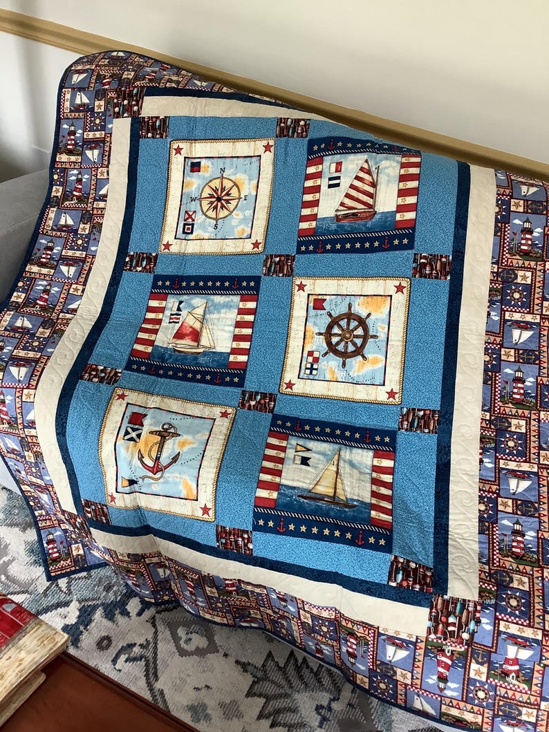 May include: A blue and white nautical themed quilt featuring a variety of images including a compass, a sailboat, an anchor, and a ship's wheel. The quilt is made with a variety of fabrics and has a white border.