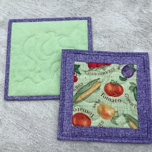 May include: Two purple-trimmed quilted pot holders. One is green with a quilted design. The other is green with a print of vegetables and the text "Green Peas, Tomato, Corn, Strawberries".