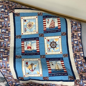 May include: A blue and white nautical themed quilt featuring compass, anchor, ship's wheel, and sailboat designs. The quilt is made with a variety of fabrics and has a red, white, and blue colour scheme.