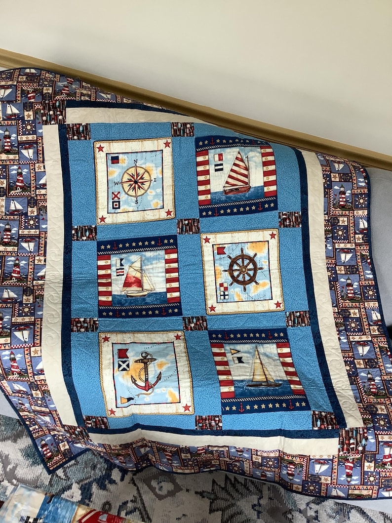 May include: A blue and white nautical themed quilt featuring compass, anchor, ship's wheel, and sailboat designs. The quilt is made with a variety of fabrics and has a red, white, and blue colour scheme.