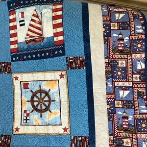 May include: A blue and white nautical themed quilt with a white border. The quilt features a sailboat, a lighthouse, a ship's wheel, and stars.