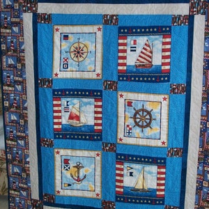May include: A blue and white nautical themed quilt with six squares featuring images of a compass, sailboat, anchor, and steering wheel. The quilt is surrounded by a border of red, white and blue nautical patterns.