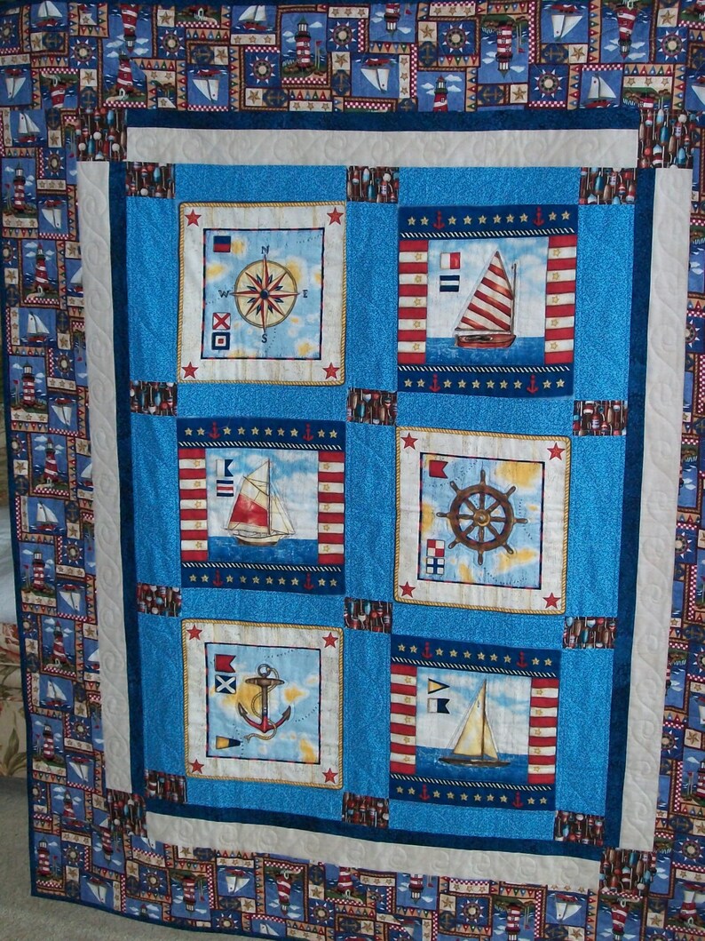 May include: A blue and white nautical themed quilt with six squares featuring images of a compass, sailboat, anchor, and steering wheel. The quilt is surrounded by a border of red, white and blue nautical patterns.