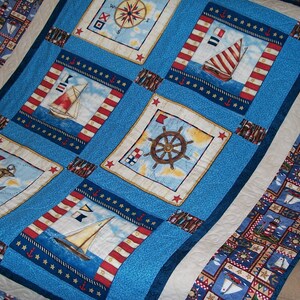 May include: A blue and white quilt with a nautical theme. The quilt features a compass, ships, anchors, and stars. The quilt is made of cotton fabric and is quilted with a white thread.