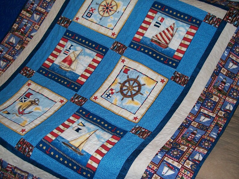 May include: A blue and white quilt with a nautical theme. The quilt features a compass, ships, anchors, and stars. The quilt is made of cotton fabric and is quilted with a white thread.