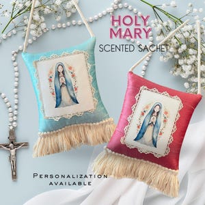 May include: Two small, square, fabric sachets with a fringe border. The sachets are blue and red and feature an image of the Virgin Mary. The text "HOLY MARY SCENTED SACHET" is printed above the sachets. The text "PERSONALIZATION AVAILABLE" is printed below the sachets.