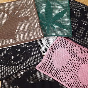 Könnte beinhalten: Eine Sammlung gehäkelter quadratischer Dekorationen in verschiedenen Farben, darunter Braun, Grün, Schwarz, Weiß und Rosa. Jedes Stück zeigt ein anderes Design, wie einen Hirsch, ein Cannabisblatt und Kopfhörer.