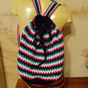 May include: A handmade crochet backpack with a drawstring closure, featuring a striped pattern in black, white, teal, and pink. The straps are pink and black. The matching shorts are multi-colored.