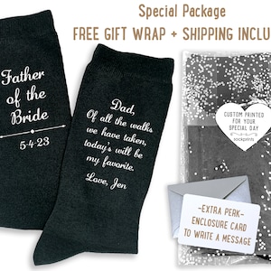 May include: A pair of black socks with white text. One sock says "Father of the Bride 5-4-23". The other sock says "Dad, Of all the walks we have taken, today's will be my favorite. Love, Jen". The socks are packaged in a clear plastic bag with a white heart-shaped tag that says "Custom Printed for Your Special Day sockprints".