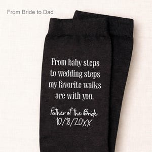 May include: Black socks with white text. The text reads "From baby steps to wedding steps my favorite walks are with you. Father of the Bride 10/18/20XX". The top of the socks reads "From Bride to Dad".