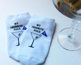 May include: A pair of white socks with a martini glass graphic and the text "My Favorite Hole" and "19" on each sock.