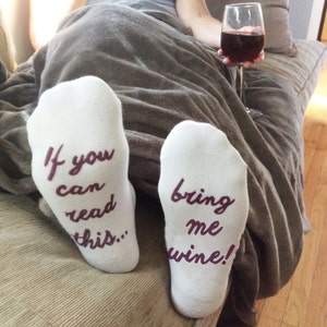 May include: A pair of white socks with purple text. One sock says "If you can read this..." and the other sock says "bring me wine!"