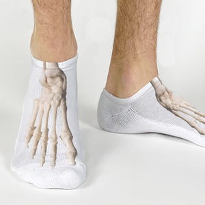 May include: White ankle socks with a detailed anatomical illustration of a foot skeleton. The socks feature a realistic bone structure design, perfect for medical students or anyone with an interest in anatomy.