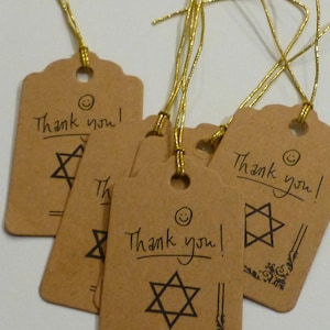 May include: Kraft paper gift tags with gold string. Each tag has the words "Thank you!" and a Star of David symbol. Some tags have a small floral design in the corner. The tags are a light brown color.