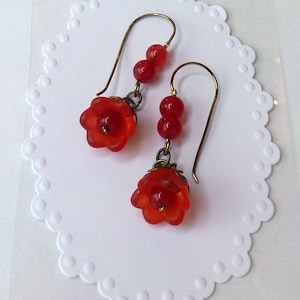 May include: A pair of red glass flower earrings with red glass beads hanging from the bottom. The earrings are on a white background.