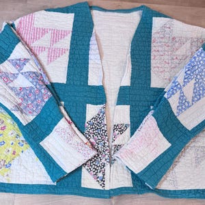 May include: A quilted jacket featuring a patchwork design with teal solid fabric borders. The garment includes various patterned squares in shades of pink, blue, yellow, and black, all finished with a consistent grid-like stitching pattern throughout.