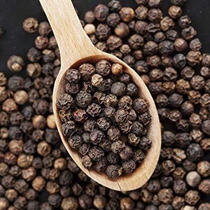 May include: A wooden spoon filled with whole black peppercorns, with more peppercorns scattered around it. The peppercorns are dark brown and round, and the spoon is light brown.