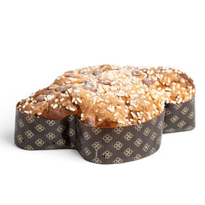 Op de afbeelding: Een traditionele Italiaanse Colomba-cake, in de vorm van een duif, staat op een witte ondergrond. De gebakken cake is goudbruin, gegarneerd met amandelen en suikerstrooisel. Het is verpakt in decoratief papier met een bloemenpatroon.