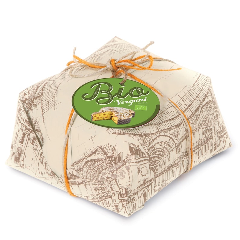 Op de afbeelding: Een vierkant verpakt voedingsmiddel, vastgebonden met oranje touw. Het inpakpapier heeft een gedetailleerd architectonisch ontwerp. Een groen ovaal label met het woord "Bio" en "Vergani" is bevestigd.