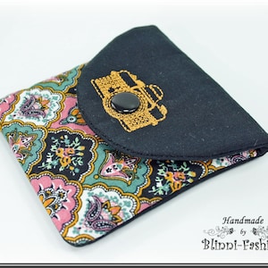 Può includere: Una piccola borsa in tessuto nero con chiusura a lembo e un design di macchina fotografica ricamato in oro. La borsa ha un motivo paisley all'esterno.