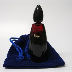 以下が含まれることがあります： 黒いキャップと「Venise」と刻まれた金色のラベルが付いた、濃い赤色のガラス製の香水瓶。瓶は青いベルベットの袋の上に置かれている。