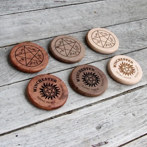 May include: Five wooden coasters with a Supernatural theme. The coasters feature the Winchester symbol, a pentagram, and the text "Saving People, Hunting Things".