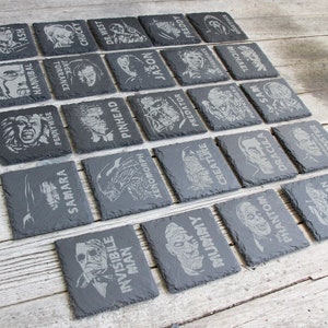 May include: A set of 25 black slate coasters with various horror movie characters and names engraved on them. The characters include Jason, Freddy, Pennywise, Dracula, and more.