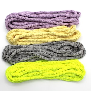 May include: Four skeins of colorful rope in shades of purple, yellow, gray, and neon green, arranged horizontally against a white background. The rope appears to be made of a knitted or woven material.