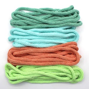 May include: Four bundles of colorful knitted rope in shades of green, blue, orange, and lime green. The ropes are arranged horizontally against a white background. The knitted texture is visible, suggesting a craft or DIY project.