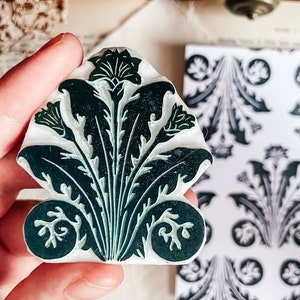 May include: A green and white rubber stamp with a floral design. The stamp is shaped like a fan and has a detailed design of leaves and flowers.