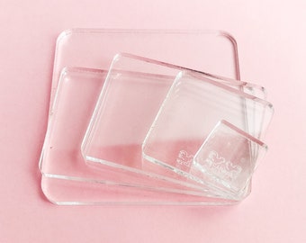 Könnte beinhalten: Vier transparente Acryl-Stempelblöcke in verschiedenen Größen, übereinander gestapelt. Die Blöcke sind quadratisch und haben eine glatte, polierte Oberfläche. Der kleinste Block hat den Text "Mycrafty" aufgedruckt.