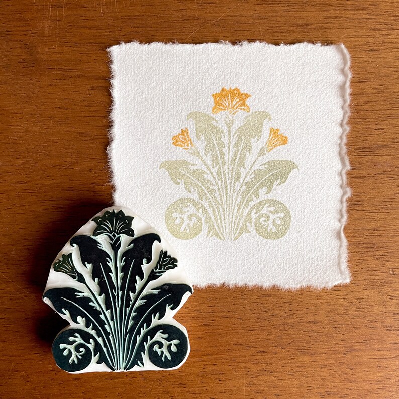 May include: A black and green rubber stamp with a floral design. The stamp is shaped like a flower with a central stem and leaves. The design is intricate and detailed.