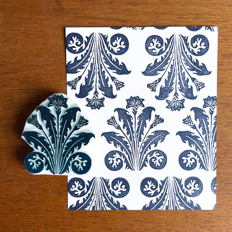 May include: A white card with a repeating pattern of dark blue stylized floral designs. A dark blue rubber stamp with a similar design is shown next to the card.