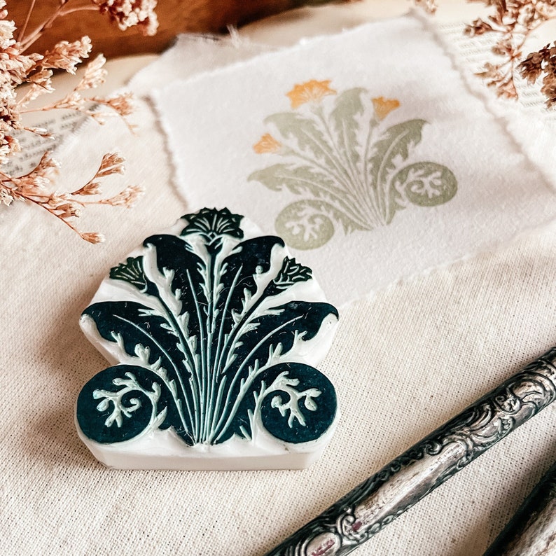 May include: A green and white floral design carved into a wooden block. The block is used for stamping designs onto fabric or paper.