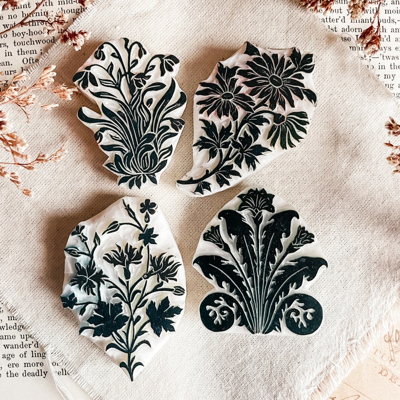 May include: Four vintage floral design rubber stamps. The stamps are white with black floral designs. The stamps are on a beige fabric background.