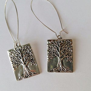 Puede incluir: Un par de pendientes de plata con un diseño de árbol de la vida. Los pendientes son de forma rectangular y tienen un cierre de gancho de alambre.