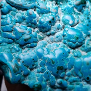 May include: A close-up of a blue and green gemstone with a unique, bubbly texture. The stone has a variety of shades of blue and green, and the bubbles are of different sizes and shapes.