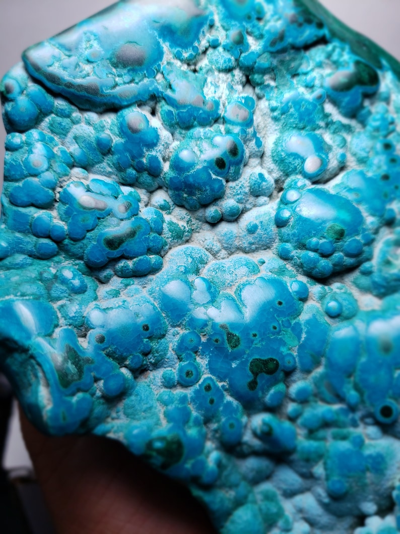 May include: A close-up of a blue and green gemstone with a unique, bubbly texture. The stone has a variety of shades of blue and green, and the bubbles are of different sizes and shapes.